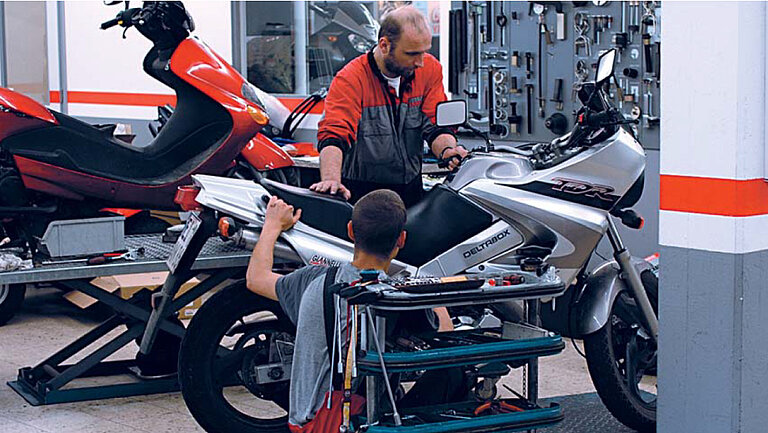 Atelier auto Imagine cu un atelier în care două persoane lucrează la o motocicletă.